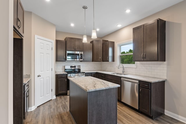 kitchen with sink, decorative light fixtures, wood-type flooring, a kitchen island, and appliances with stainless steel finishes