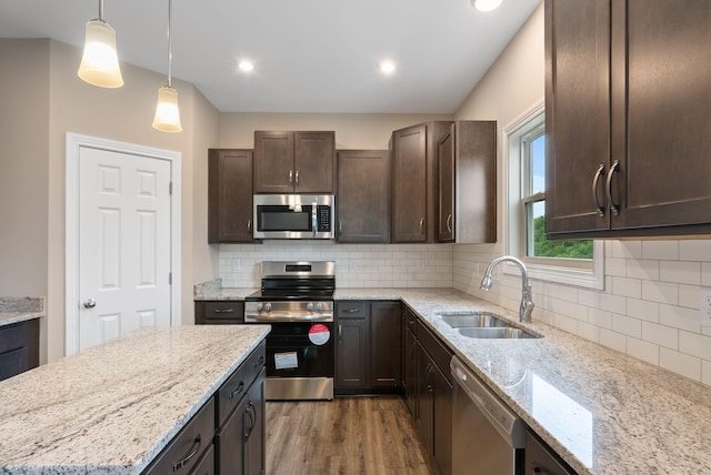 kitchen featuring stainless steel appliances, decorative light fixtures, sink, and light stone countertops