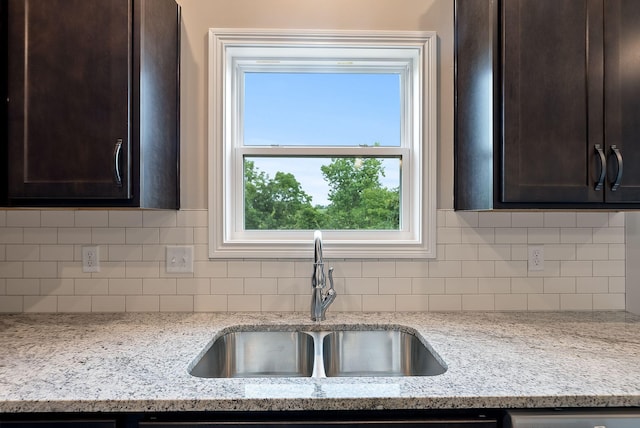 kitchen with light stone countertops, dark brown cabinets, tasteful backsplash, and sink