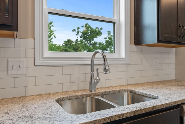 interior details featuring sink, backsplash, light stone countertops, and dark brown cabinetry