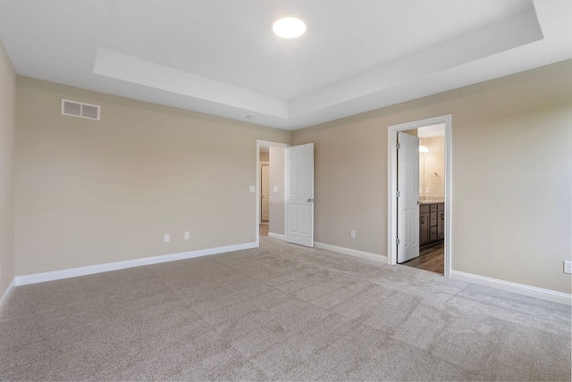 unfurnished bedroom featuring ensuite bathroom, a tray ceiling, and carpet flooring