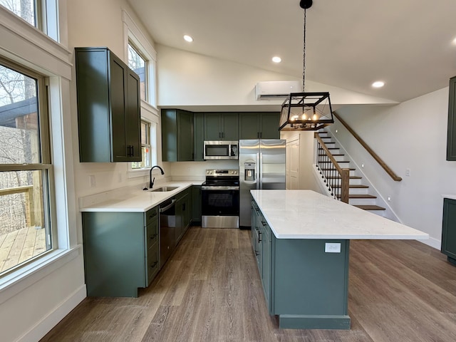 kitchen with a kitchen island, a sink, light countertops, appliances with stainless steel finishes, and decorative light fixtures