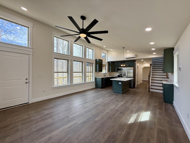 kitchen with pendant lighting, light countertops, appliances with stainless steel finishes, open floor plan, and a kitchen island with sink
