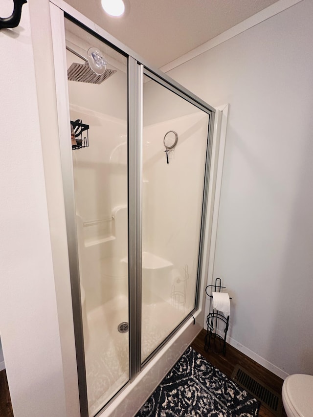 bathroom with hardwood / wood-style floors, toilet, and an enclosed shower