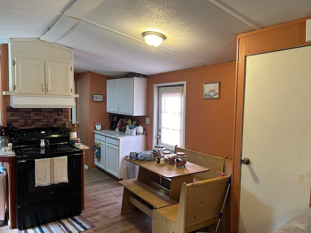 kitchen featuring black electric range, wood-type flooring, white cabinets, and vaulted ceiling