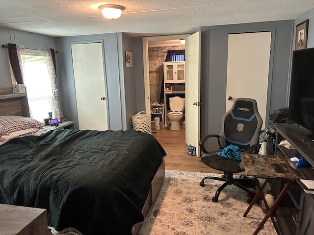 bedroom featuring a textured ceiling, light wood-type flooring, and connected bathroom