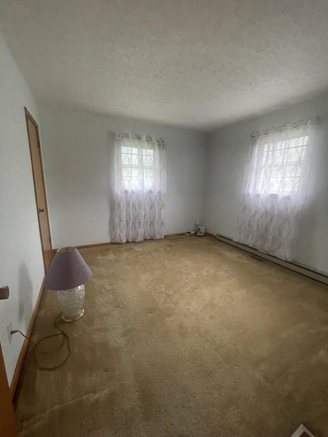 empty room with carpet floors, a textured ceiling, and a baseboard heating unit