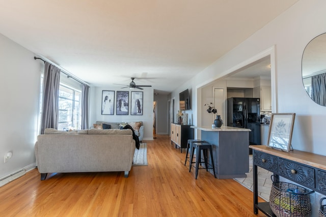 living room with ceiling fan, a baseboard heating unit, and light wood-type flooring