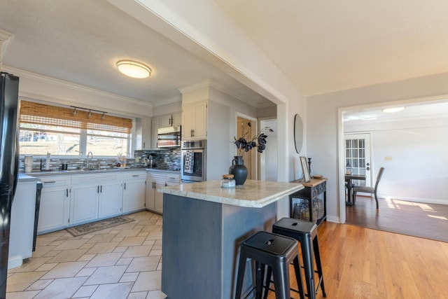 kitchen featuring sink, appliances with stainless steel finishes, white cabinetry, a kitchen bar, and decorative backsplash