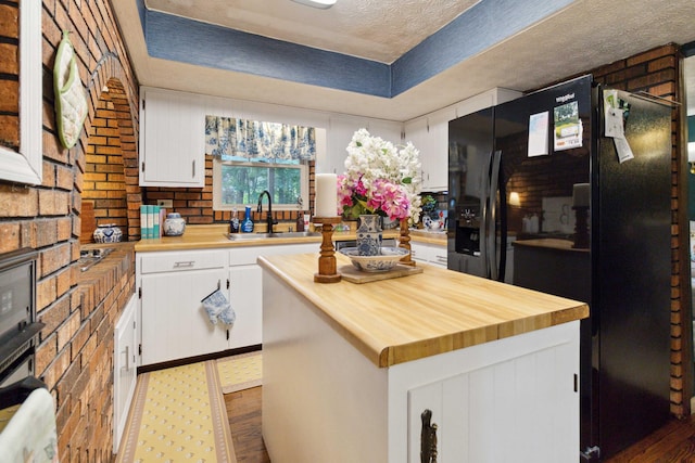 kitchen featuring sink, white cabinets, a center island, black fridge, and a textured ceiling