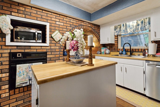 kitchen featuring sink, appliances with stainless steel finishes, a center island, white cabinets, and brick wall