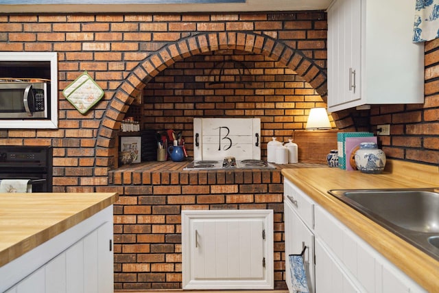 kitchen featuring wooden counters, brick wall, sink, and white cabinets