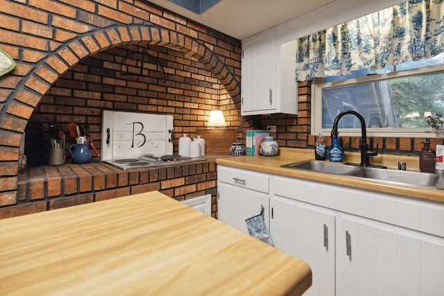 kitchen with sink, gas cooktop, white cabinets, brick wall, and wood counters