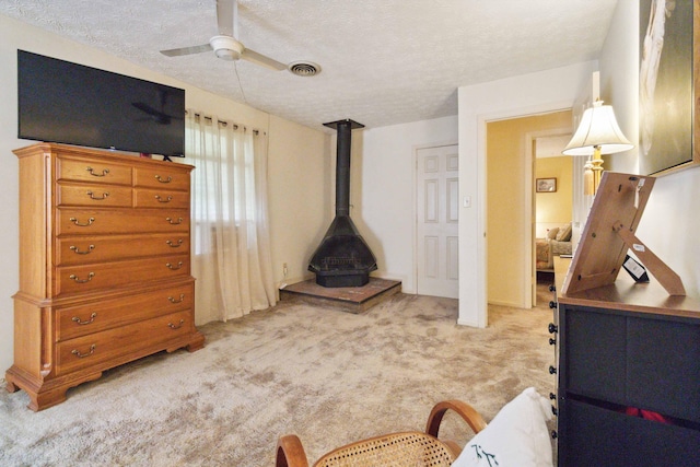 living room with a wood stove, light colored carpet, a textured ceiling, and ceiling fan