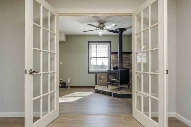 unfurnished office featuring french doors, a textured ceiling, a wood stove, ceiling fan, and light hardwood / wood-style floors