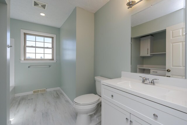 bathroom featuring hardwood / wood-style flooring, vanity, toilet, and a textured ceiling