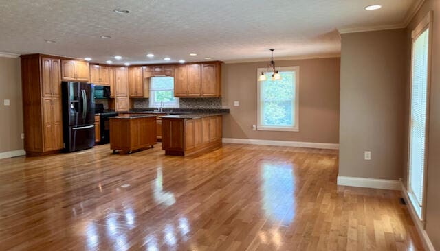 kitchen with light hardwood / wood-style flooring, black appliances, backsplash, a kitchen island, and crown molding