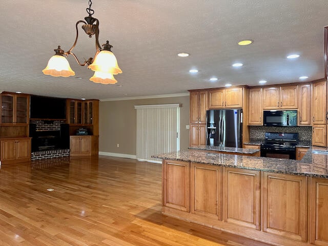 kitchen featuring decorative light fixtures, electric stove, a fireplace, stainless steel refrigerator with ice dispenser, and light wood-type flooring