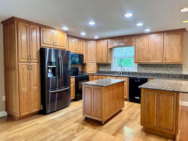 kitchen featuring dark stone counters, black appliances, sink, light hardwood / wood-style floors, and a kitchen island