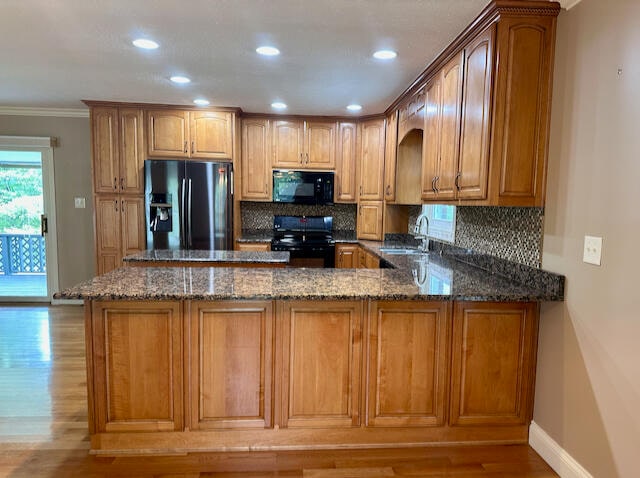 kitchen featuring dark stone counters, stainless steel refrigerator with ice dispenser, light wood-type flooring, range with electric cooktop, and kitchen peninsula