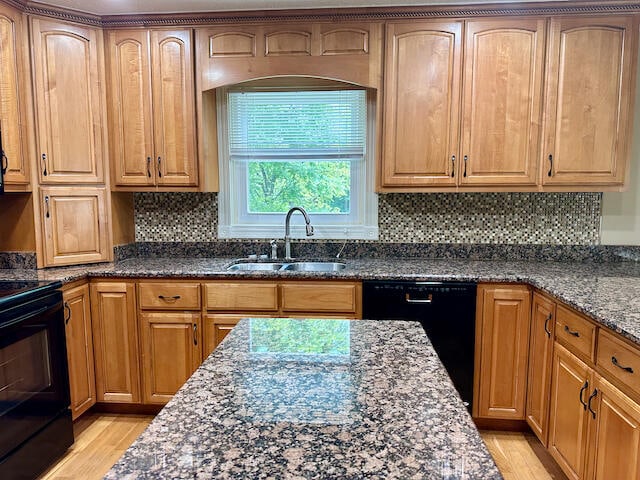 kitchen featuring dark stone countertops, light hardwood / wood-style flooring, tasteful backsplash, black appliances, and sink