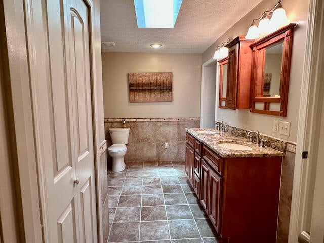 bathroom with double vanity, a textured ceiling, tile patterned floors, a skylight, and toilet