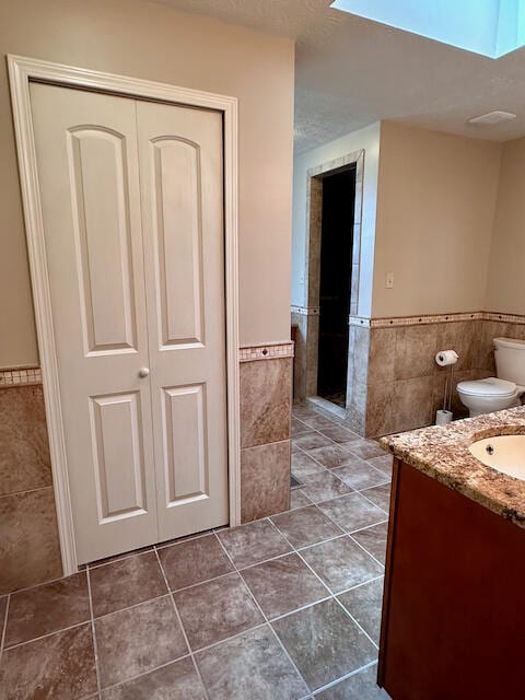 bathroom featuring vanity, toilet, tile patterned flooring, and tile walls