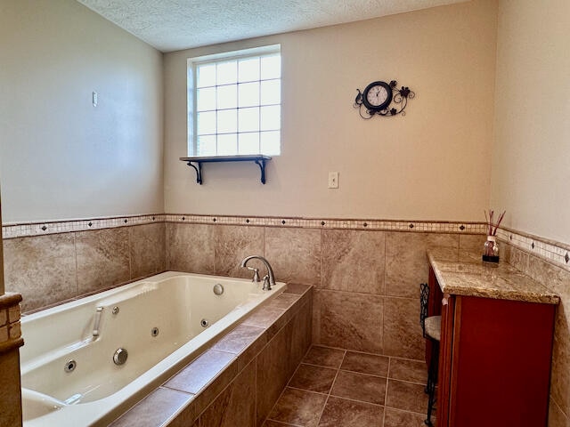 bathroom featuring a relaxing tiled tub, a textured ceiling, tile walls, and tile patterned flooring