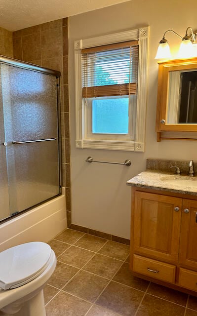 full bathroom with vanity, shower / bath combination with glass door, toilet, a textured ceiling, and tile patterned flooring