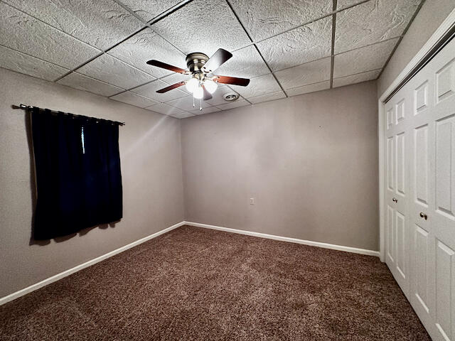 unfurnished bedroom with a closet, carpet floors, ceiling fan, and a paneled ceiling