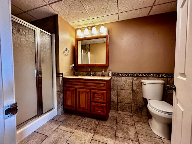 bathroom featuring tile walls, tile patterned flooring, toilet, a drop ceiling, and vanity