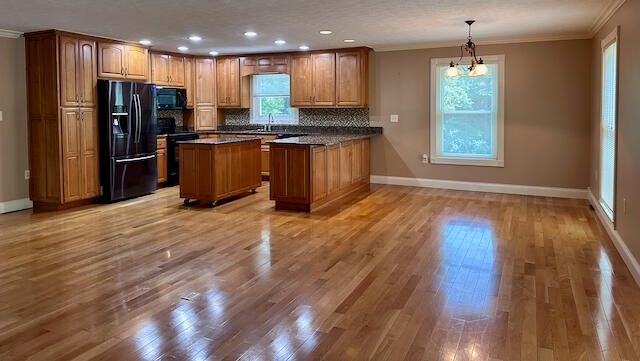 kitchen with black appliances, tasteful backsplash, crown molding, light wood-type flooring, and a kitchen island