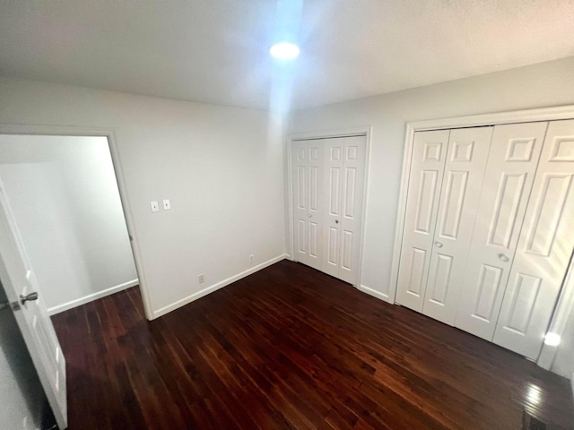 unfurnished bedroom featuring dark hardwood / wood-style floors and multiple closets