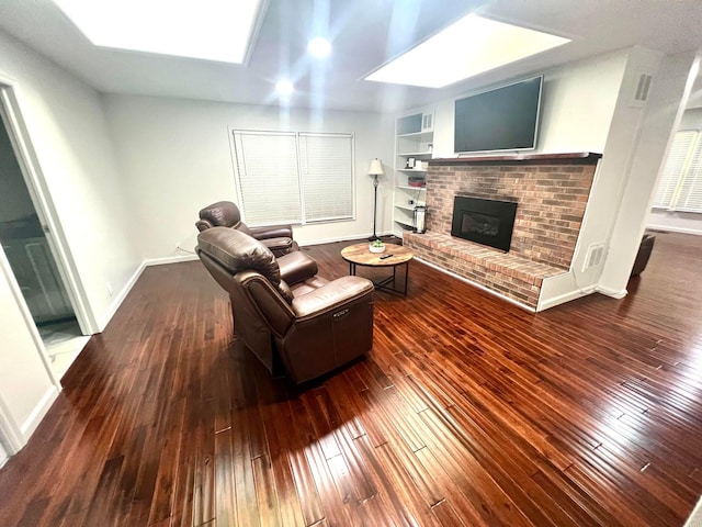 living room with a skylight, built in features, dark wood-type flooring, and a fireplace