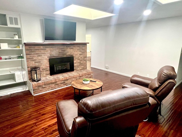 living room with a skylight, built in shelves, dark hardwood / wood-style floors, and a brick fireplace