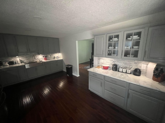 kitchen featuring sink, dark hardwood / wood-style floors, a textured ceiling, gray cabinets, and decorative backsplash