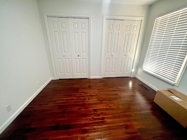 unfurnished bedroom featuring dark wood-type flooring and two closets