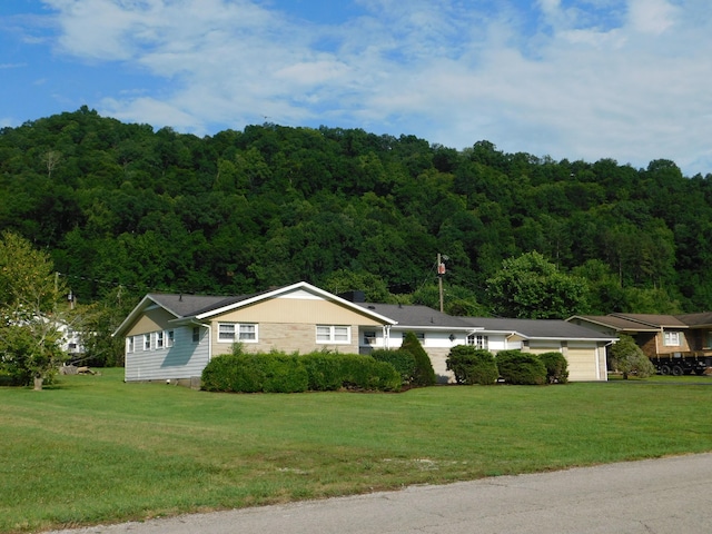 ranch-style home with a forest view, an attached garage, and a front yard