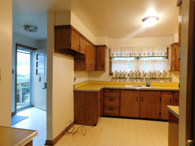 kitchen featuring baseboards, brown cabinets, light countertops, light floors, and a sink