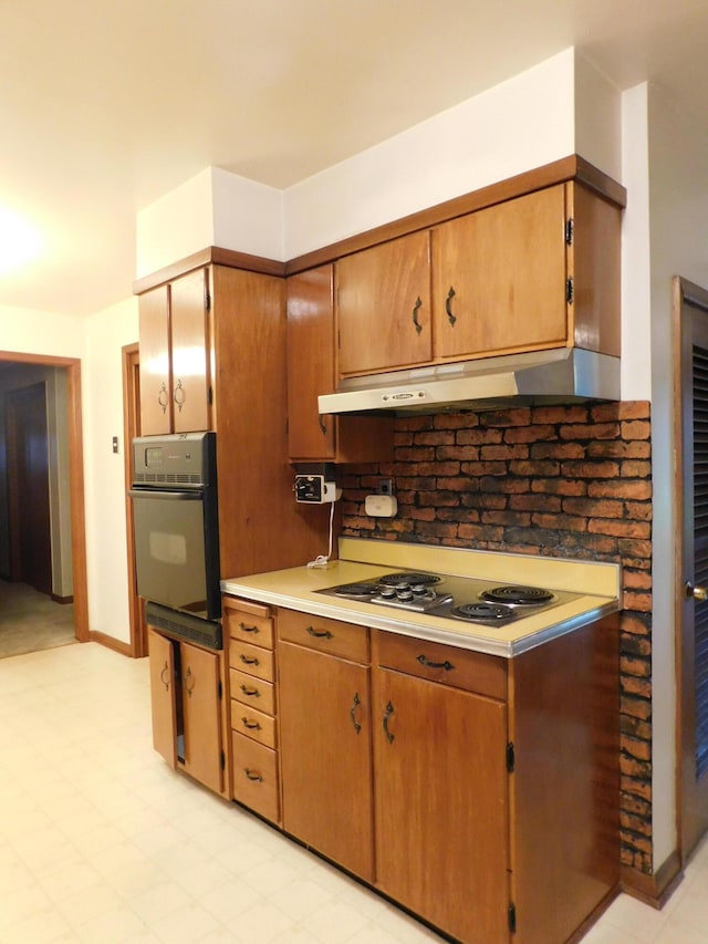 kitchen with brown cabinetry, oven, light countertops, under cabinet range hood, and stainless steel electric stovetop