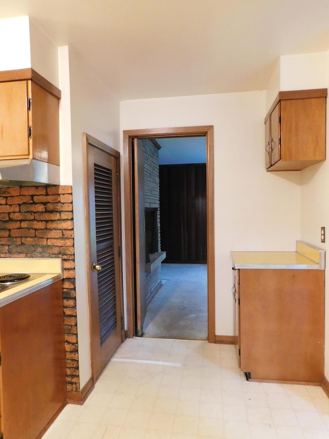 kitchen featuring brown cabinetry, under cabinet range hood, light countertops, light floors, and a fireplace