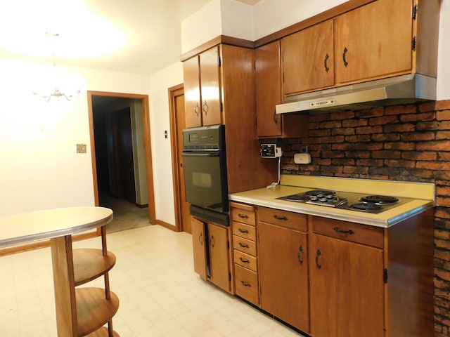 kitchen with electric stovetop, oven, an inviting chandelier, light countertops, and under cabinet range hood