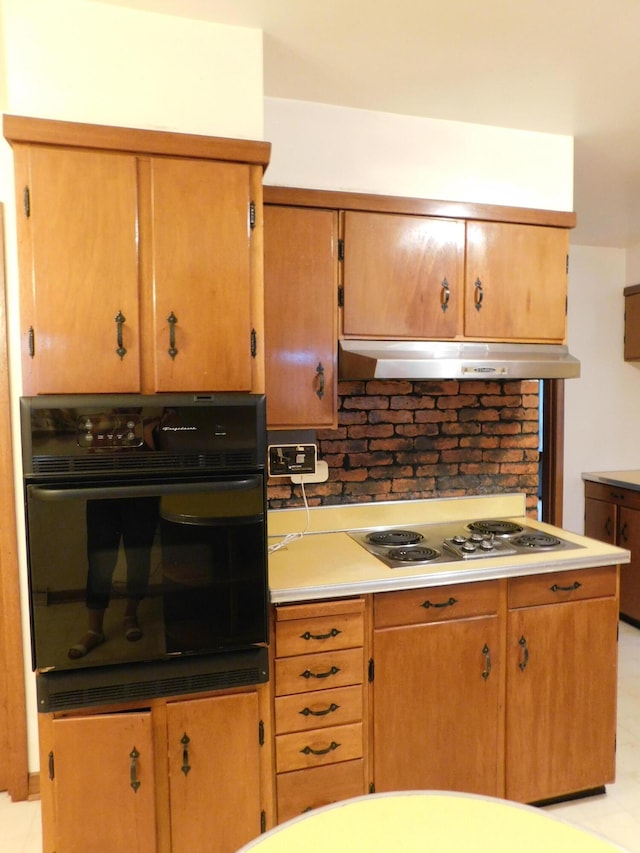 kitchen featuring under cabinet range hood, stainless steel electric cooktop, black oven, light countertops, and tasteful backsplash