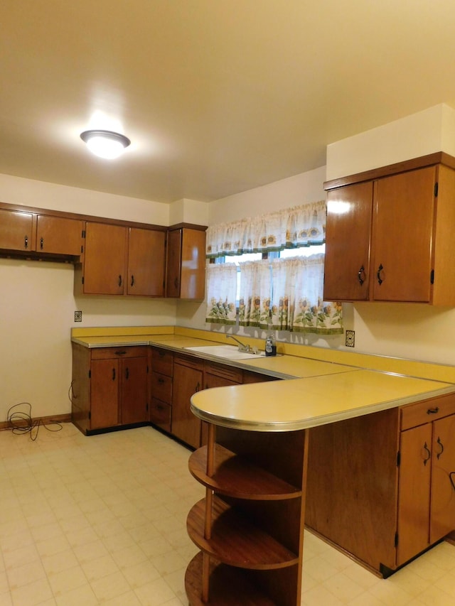 kitchen with a peninsula, light countertops, light floors, open shelves, and a sink