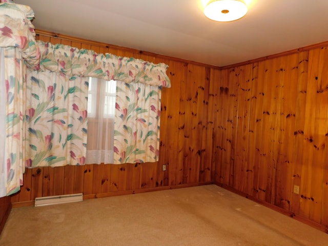 carpeted spare room featuring a baseboard heating unit, wooden walls, and baseboards