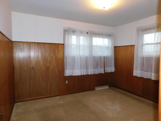 empty room with a baseboard heating unit, wainscoting, wood walls, and plenty of natural light