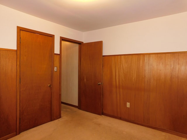 unfurnished bedroom featuring wooden walls, light colored carpet, a closet, and wainscoting