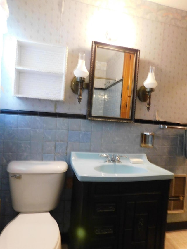 bathroom with wainscoting, vanity, toilet, and wallpapered walls