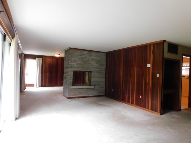 unfurnished living room featuring wooden walls, light carpet, and a stone fireplace