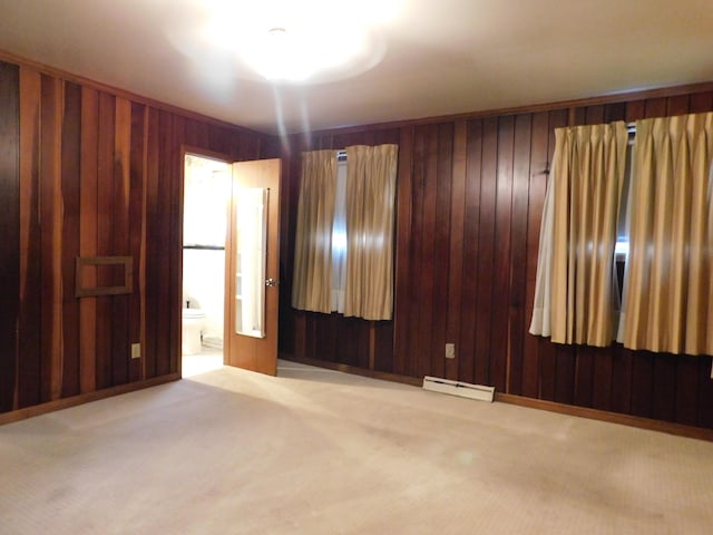 carpeted spare room with a baseboard heating unit, baseboards, and wooden walls